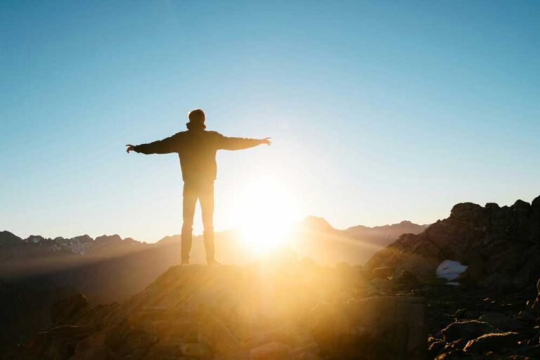 Person standing on a mountain peak at sunrise, representing self-improvement and personal growth